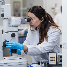 woman looking into microscope in lab