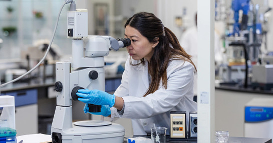 woman looking into microscope in lab
